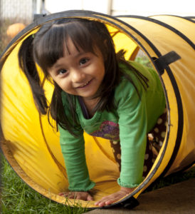 Small girl smiling and siting playfully in a pipe