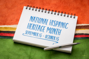 A photo of a notebook laying on a brightly colored background that someone has written National Hispanic Heritage Month September 15 to October 15