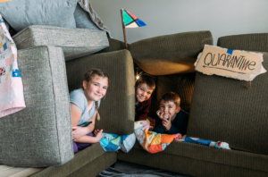 Kids play in a pillow fort with a cardboard sign tapped to it the says "Quarantine"