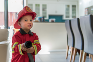 Small child dressed as a fire fighter is holding a toy hose.