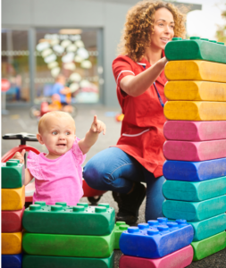 A child care provider stacks over-sized Lego blocks with a young child