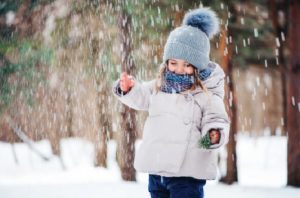 A little girl in a snow coat, hat and scarf is giggling as snow falls around her.